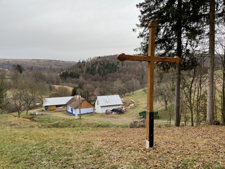 Kříž shlíží na soubor lidových staveb ve vesničce Žítková